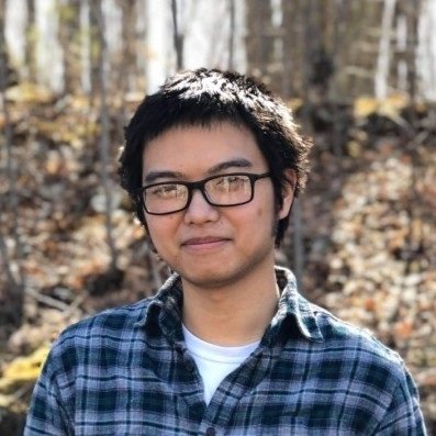 Portrait headshot of Matthew "FlyAwayNow" Nguyen, writer for the video game Project Wingman, wearing glasses and a plaid button-up shirt outdoors against a blurred forest background.