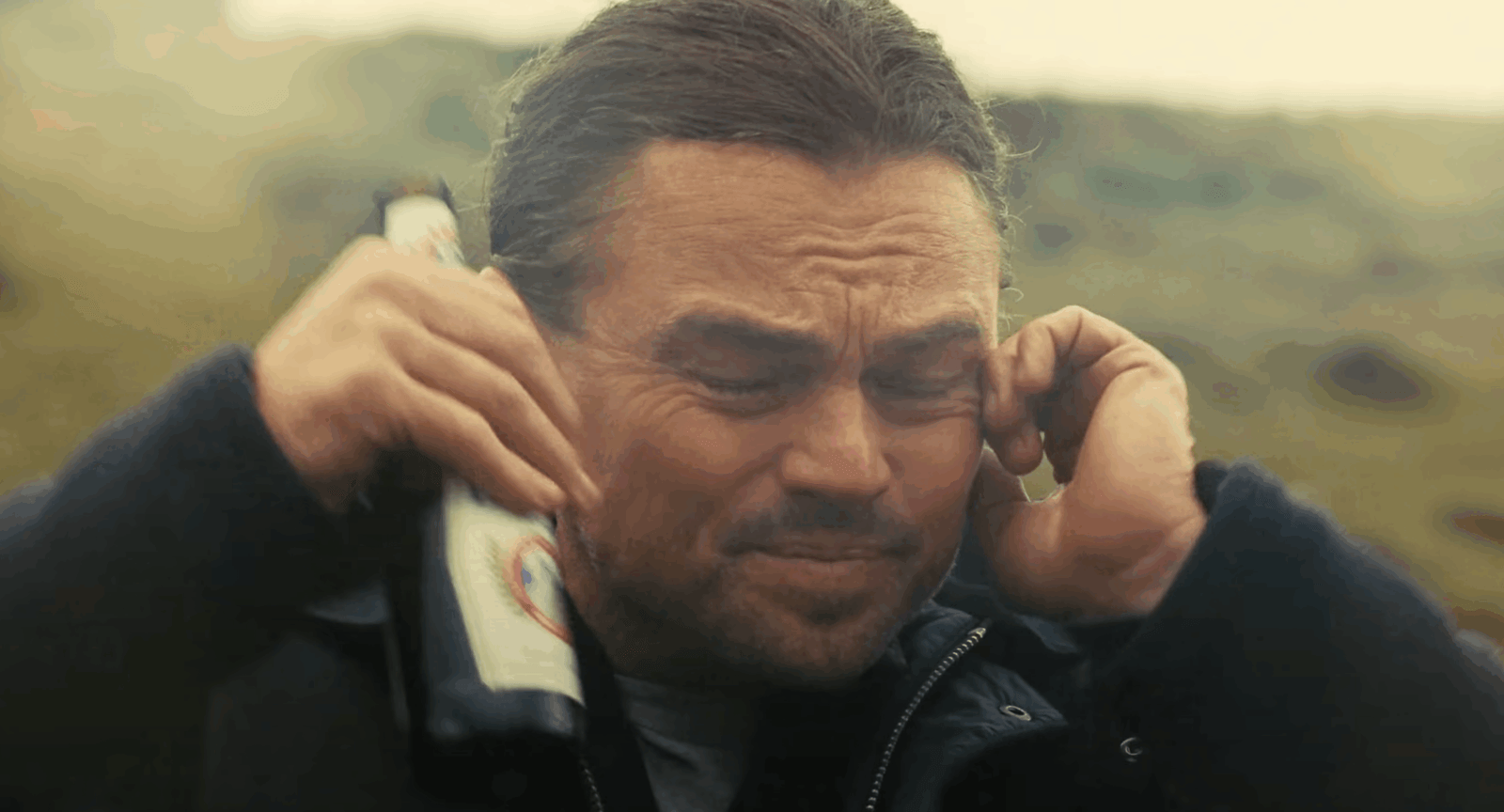 Leonardo DiCaprio holds his ears with a beer in the trailer to One Battle After Another
