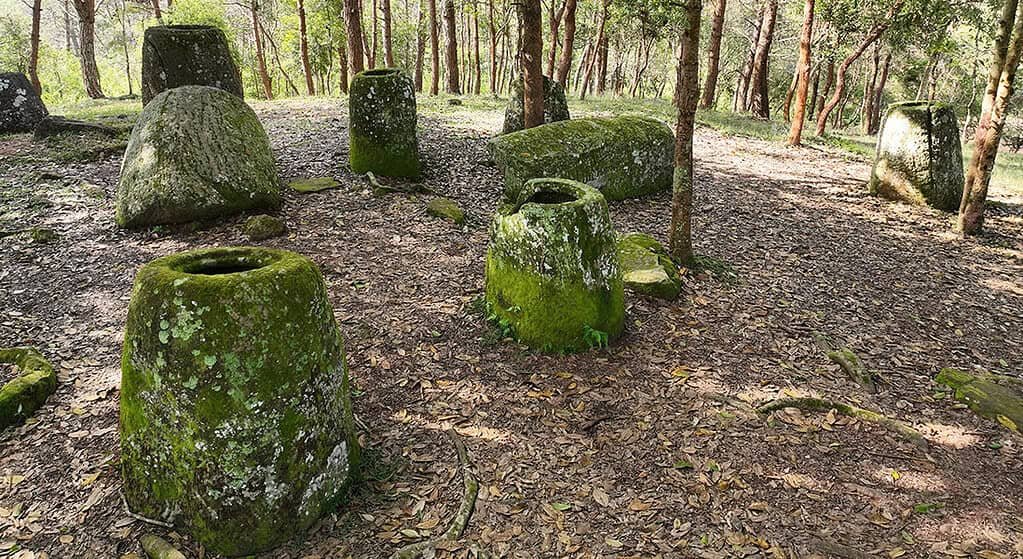 Ancient Burial Jars in Laos Have Been Running a 2,000-Year Natural Experiment 1 Ancient stone jars covered in moss scattered beneath trees in a forested area