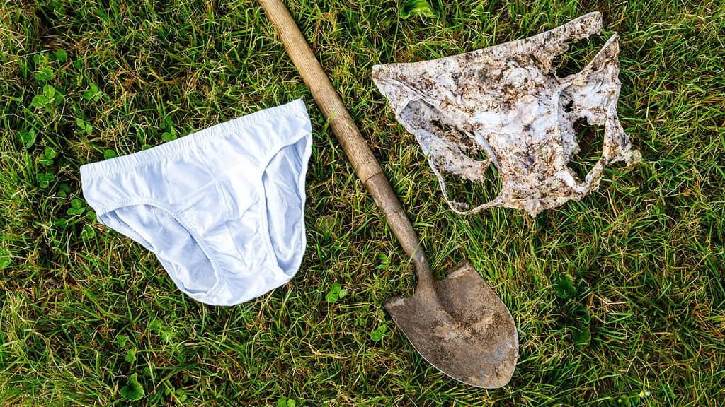 One new white pair of underwear and one decomposed cotton underwear on either side of a shovel on grass