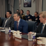 Defense Secretary Pete Hegseth sitting at a large conference table surrounded by civilian advisors and military brass during a high-level Pentagon meeting.