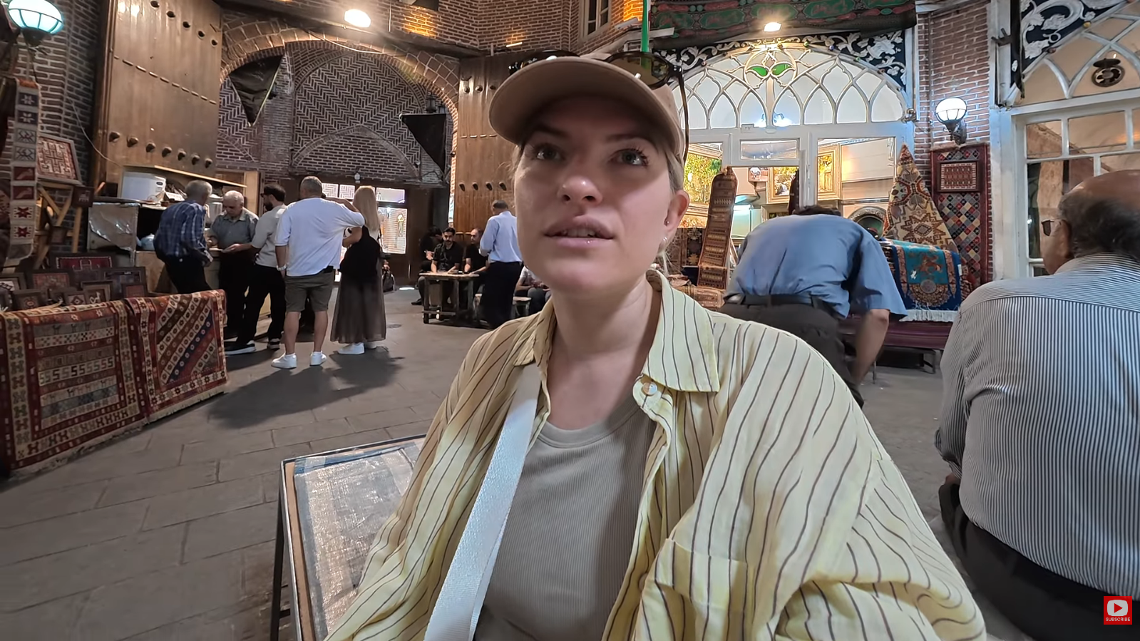 Travel Creators Matt and Julia Journey to Iran in 2026: Exploring Daily Life Beyond Headlines 1 Travel vlogger Julia sitting inside the historic covered Grand Bazaar of Tabriz, surrounded by traditional Iranian carpets and local shoppers.