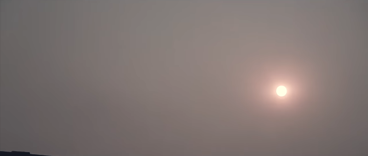 Dim bright sun glowing through a dense layer of grey haze and smog in a pale sky
