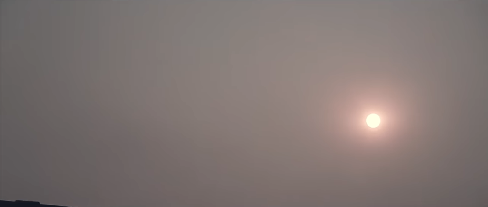 Dim bright sun glowing through a dense layer of grey haze and smog in a pale sky