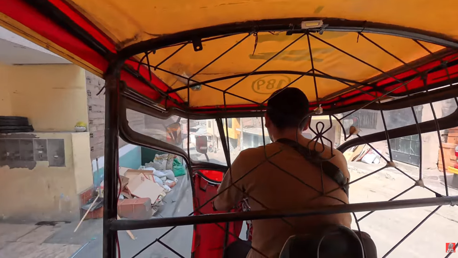 View from inside a traditional Peruvian mototaxi showing the driver operating the vehicle through the streets of San Juan de Lurigancho in Lima, Peru.