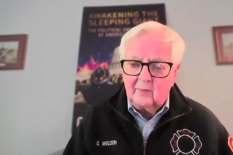 Former Congressman Kurt Weldon speaking during a video interview wearing a black embroidered firefighter jacket.