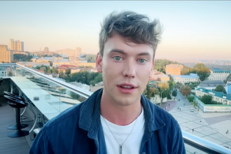 Selfie portrait of British YouTuber Caolan Robertson outdoors with city architecture and a bridge in the background in Kyiv, Ukraine.