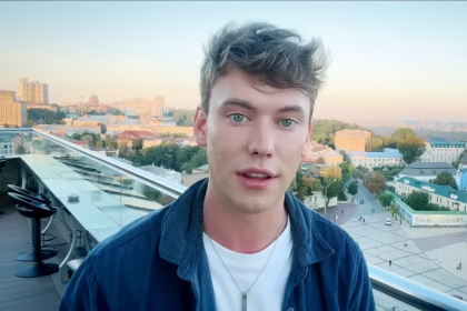 Selfie portrait of British YouTuber Caolan Robertson outdoors with city architecture and a bridge in the background in Kyiv, Ukraine.