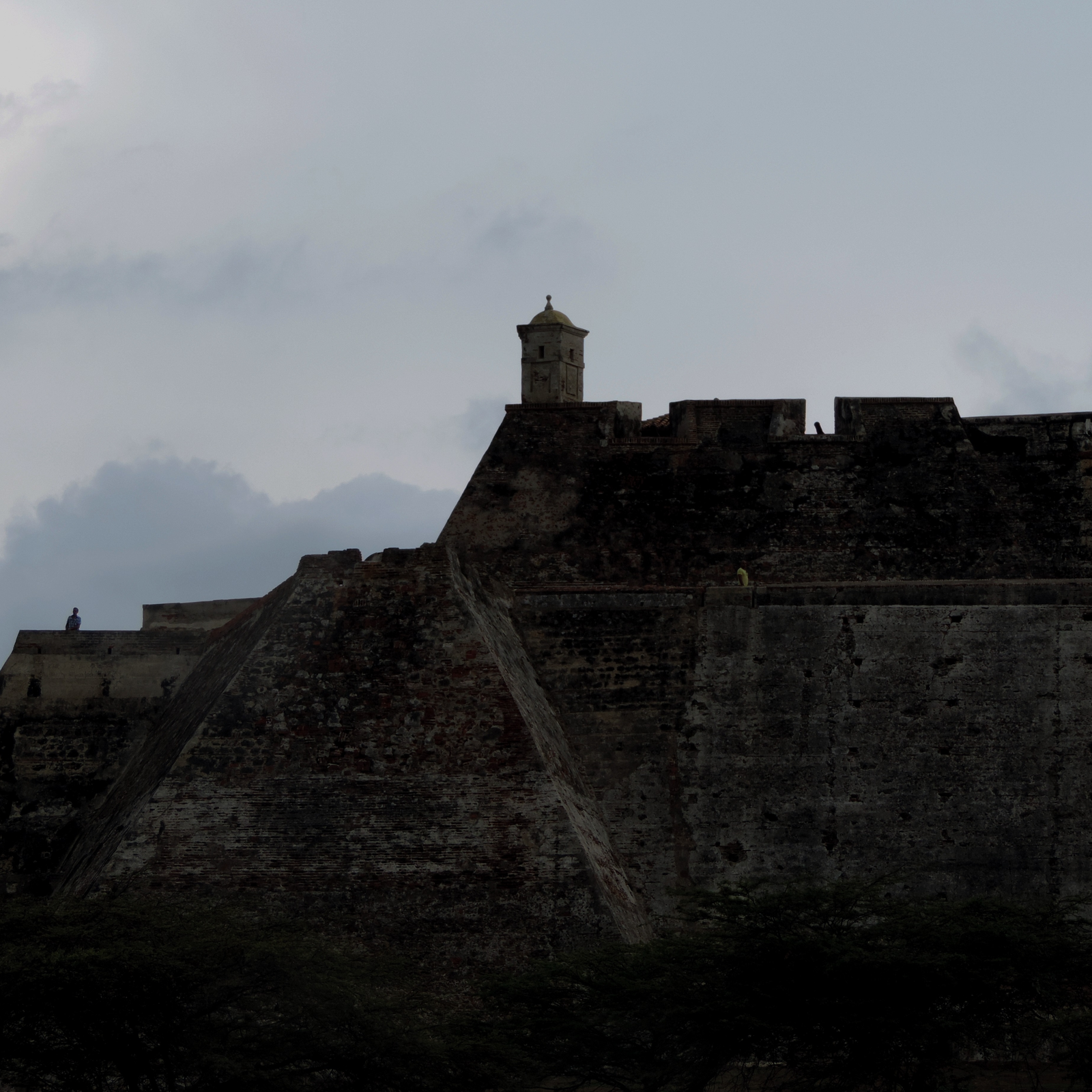 Low-angle view of the stone ramparts and watchtower of Castillo San Felipe de Barajas against a moody sky in Cartagena, Colombia.